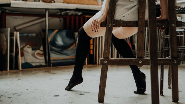 Woman painter legs on the floor. Art studio interior. Drawing supplies, oil paints, artist brushes