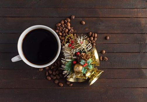 A cup of coffee, coffee beans and Christmas toy with three golden bells on wooden background.Christmas concept.