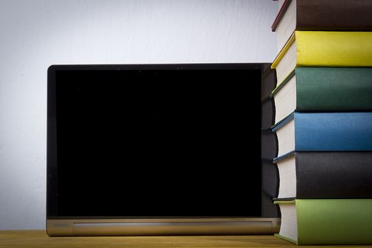 Stack of books with multi-colored binders and a tablet on a wooden table