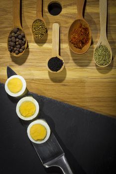 Spices in wooden spoons and eggs on a stone cutting board