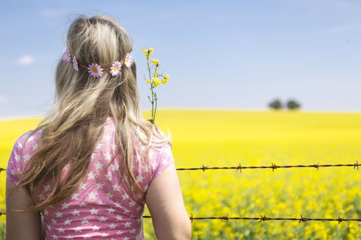 Woman at barbed wire fence looking at canola field flowering  in spring time. Shallow depth of field with soft blur for copy.