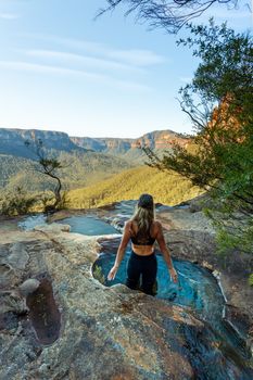 Female standing in plunge pools eroded into the rock ledge at the end of the canyon, where the creek flows off the cliff ledge 70 metres below into the valley and beyond.