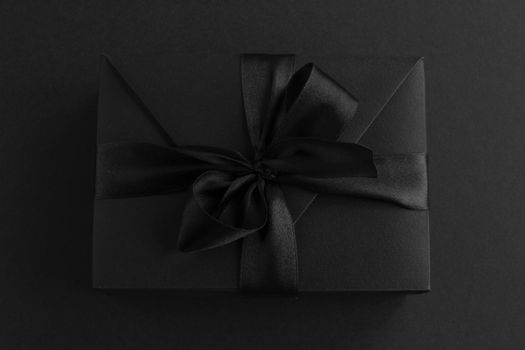 Black friday gift, paper box with silk ribbon bow on black paper background with copy space for text, flat lay top view template