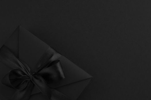 Black friday gift, paper box with silk ribbon bow on black paper background with copy space for text, flat lay top view template