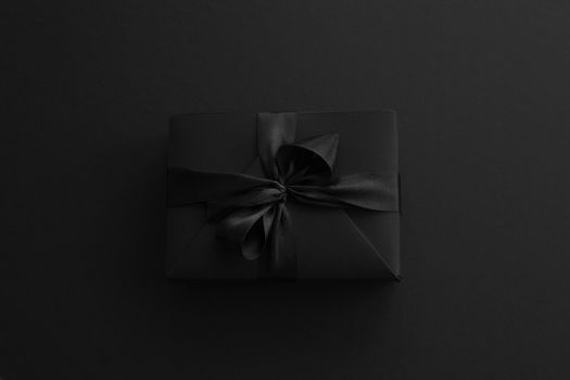 Black friday gift, paper box with silk ribbon bow on black paper background with copy space for text, flat lay top view template