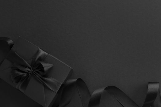 Black friday gift, paper box with silk ribbon bow on black paper background with copy space for text, flat lay top view template