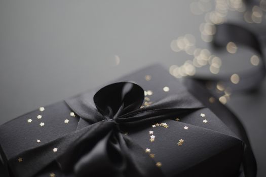 Black friday gift, paper box with silk ribbon bow on black paper background with copy space for text