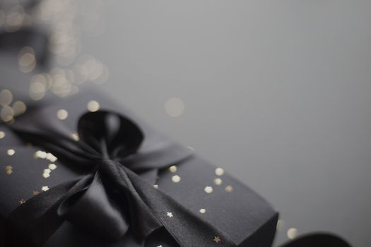 Black friday gift, paper box with silk ribbon bow on black paper background with copy space for text