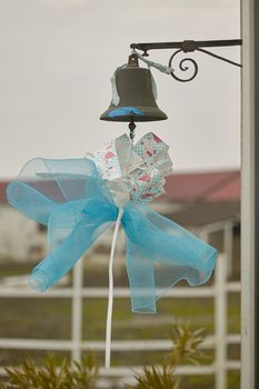 Blue bow hanging from a metal bell to symbolize the birth of a child, or to celebrate the ceremony of Catholic baptism.