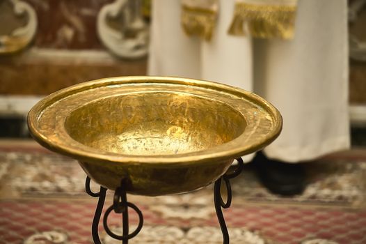 Evocative image of Catholic baptism with the golden bowl to put the holy water with which the baby will be baptized. Behind the blurred background you can see the priest ready to start the ceremony.