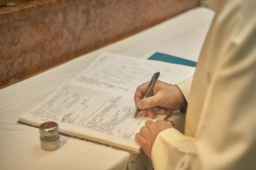 Priest as he signs the register for the baptism of a new baby during the Catholic baptism ceremony.