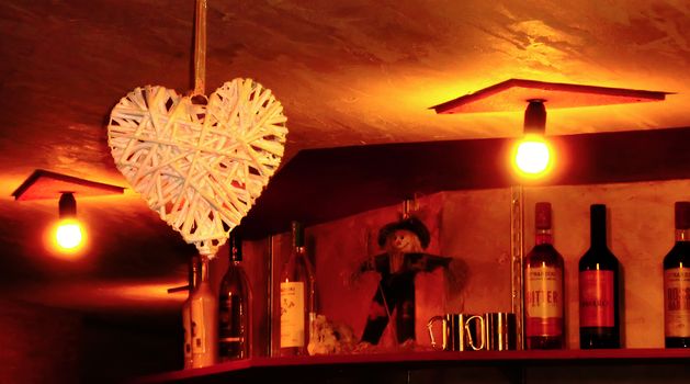 Interior of an Italian bar with wooden heart-shaped decorations and bottles of alcohol on the shelf at the bottom.