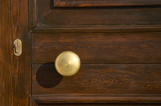 Detail of the handle and lock of a handcrafted dark wooden house door.