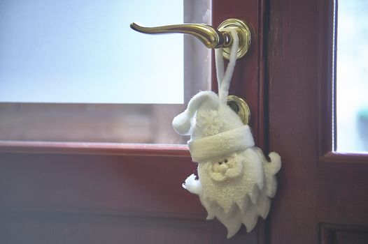 Christmas decoration in the shape of Santa Claus hanging on the door handle of the house to symbolize the arrival of Christmas.
