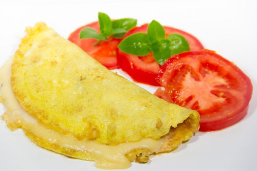 omelette made with beaten eggs stuffed with onion cheese and tomatoes on white background with sliced tomatoes and basil