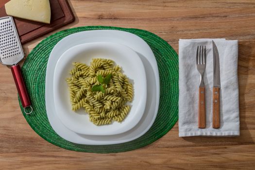 Pesto pasta in a white plate on a wooden table with rustic cutlery