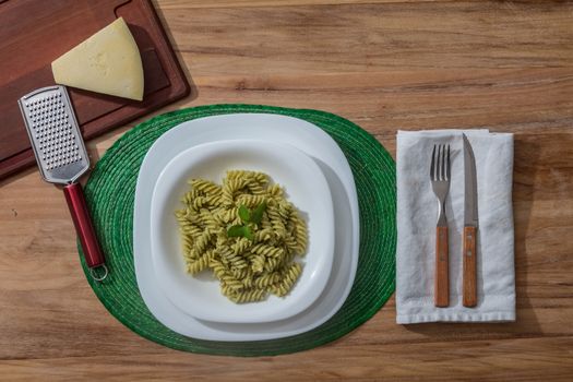 Pesto pasta in a white plate on a wooden table with rustic cutlery