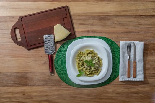 Pesto pasta in a white plate on a wooden table with rustic cutlery