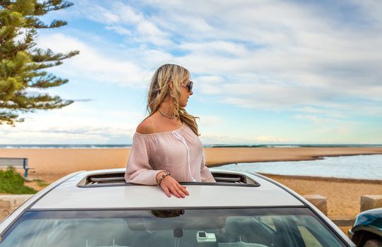 Rolad trip summer beach vibes.  Woman stand in the sunroof of her car by the beach.
 travel, transport, vacation, road trip, carefree