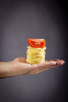 Italian pasta and a slice of tomato in a male hand