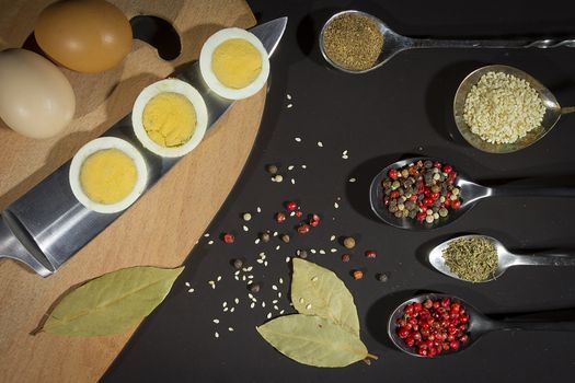 Spices in metal spoons and eggs on a cutting board