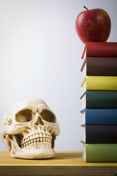 Stack of books, apple and skull on a wooden table