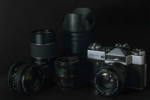 Still life with vintage photographic equipment (camera and various optics) taken in side light on black background.