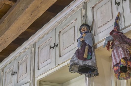 Statuettes of vintage strghe hanging from a white wooden cabinet that has been corroded by time: an example of spooky and scary decoration inside the house.