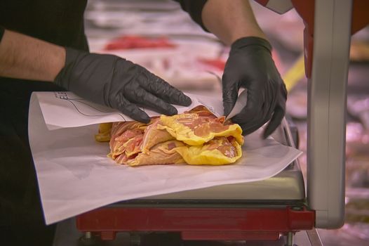 Hands weighing chicken meat on a scales at the meat department of a supermarket.