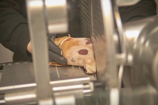 Hands of an operator at the supermarket slicing a piece of ham on an electric electrician.