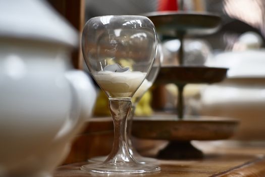 Glass with inside a candle consumed by use and other vintage ornamental objects blurred around.