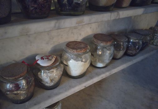 Spice shelf of an ancient kitchen full of glass jars containing precisely the same spices.