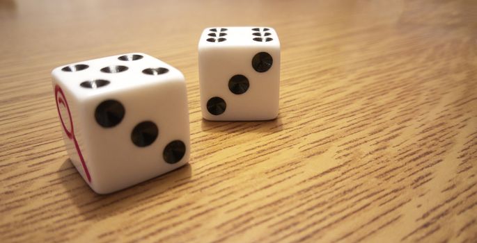 Two white playing dice with black numbers on a light wooden table.