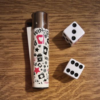 Gaming dice and lighter resting on a light wooden table.