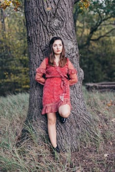 Woman standing next to a tree in park in golden autumn.
