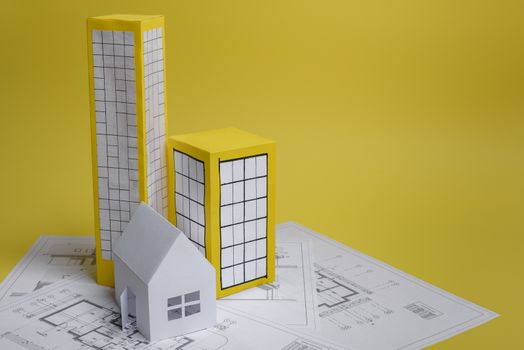 White family paper house, house projects plan and blueprints on yellow background paper. Minimalistic and simple concept, style. Vertical orientation.