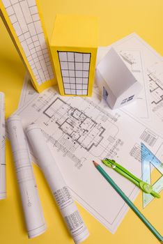 White family paper house, house projects plan and blueprints on yellow background paper. Minimalistic and simple concept, style. Vertical orientation.