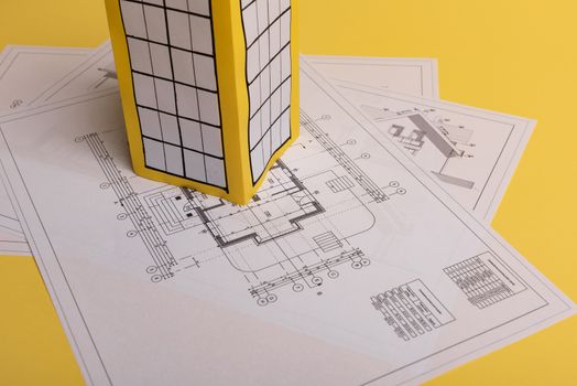 White family paper house, house projects plan and blueprints on yellow background paper. Minimalistic and simple concept, style. Vertical orientation.