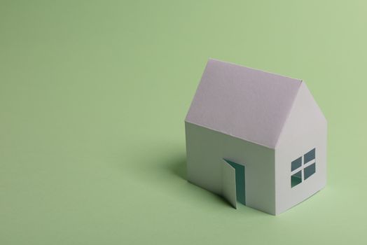 White family paper house in man hand on mint background paper. Minimalistic and simple concept, style. Copy space. Horizontal orientation