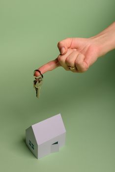 White family paper house. House keys in hand on mint background paper. Minimalistic and simple concept, style. Copy space. Vertical orientation. Family moving or removal concept.