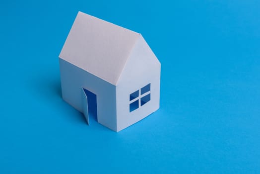 White family paper house over block of flats on blue background paper. Minimalistic and simple concept, style. Copy space. Vertical orientation.