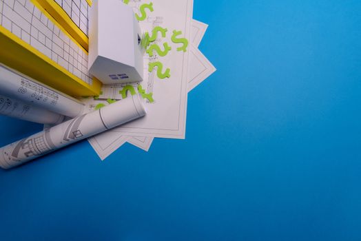 Paper skyscrapers , us dollar money, house projects plan and blueprints on blue background paper. Minimalistic and simple concept, style. Horizontal orientation. View from above. Copy space.