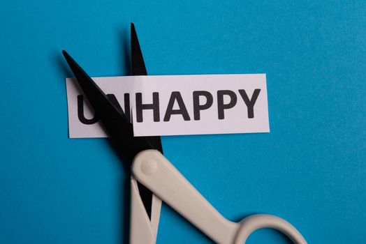 card with text unhappy, cutting word 'un' so it written 'happy'. Copy space. BLue background. Studio shoot