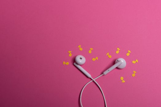 white earphones and yellow paper notes on pink background. view from above