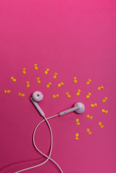 white earphones and yellow paper notes on pink background. view from above
