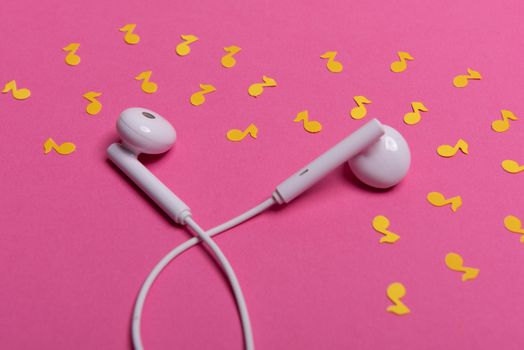 white earphones and yellow paper notes on pink background. view from above
