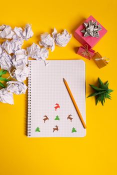 gift box and green origami trees with notepad on yellow desk, table