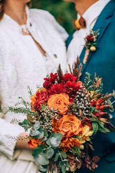 Crop blurred just married couple in elegant clothes hugging and holding beautiful bouquet of fresh colorful flowers in composition with green and brown herbs