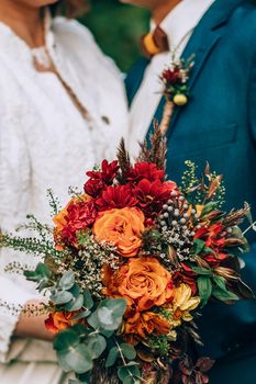 Crop blurred just married couple in elegant clothes hugging and holding beautiful bouquet of fresh colorful flowers in composition with green and brown herbs