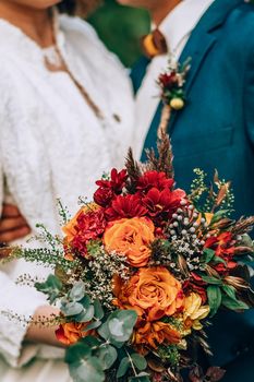 Crop blurred just married couple in elegant clothes hugging and holding beautiful bouquet of fresh colorful flowers in composition with green and brown herbs